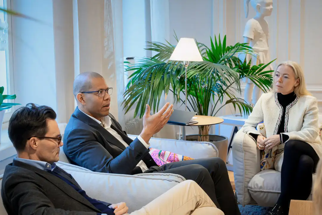 Ryhmä rentoja ihmisiä valoisassa tilassa kuuntelemassa etualalla näkyvän esiintyjän puhetta