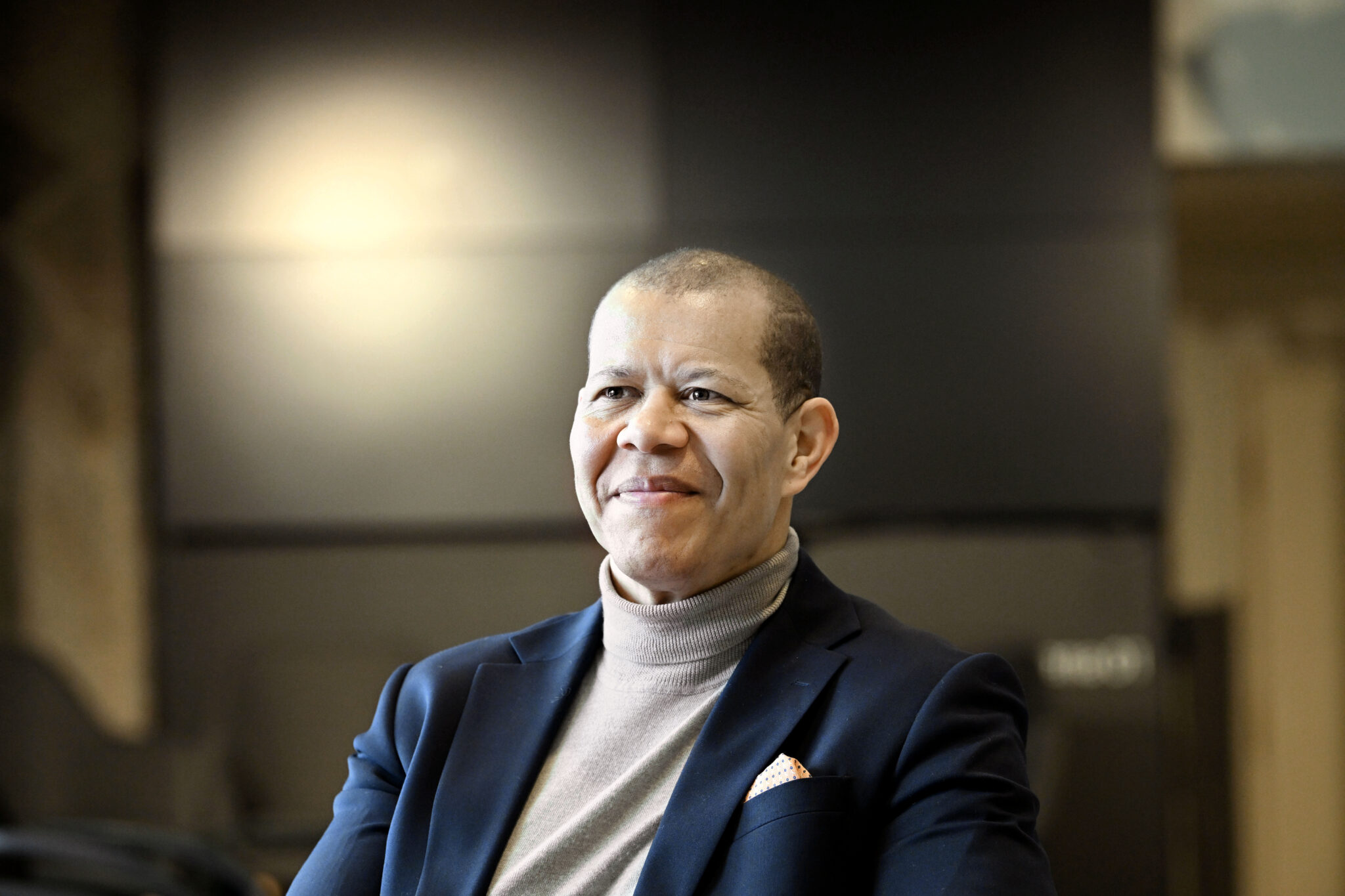A group of relaxed people in a brightly lit room listening to a speaker in the foreground